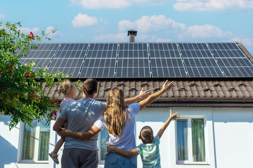 o casa cu multe panouri solare pe acoperis si o familie cu copii in fata ei