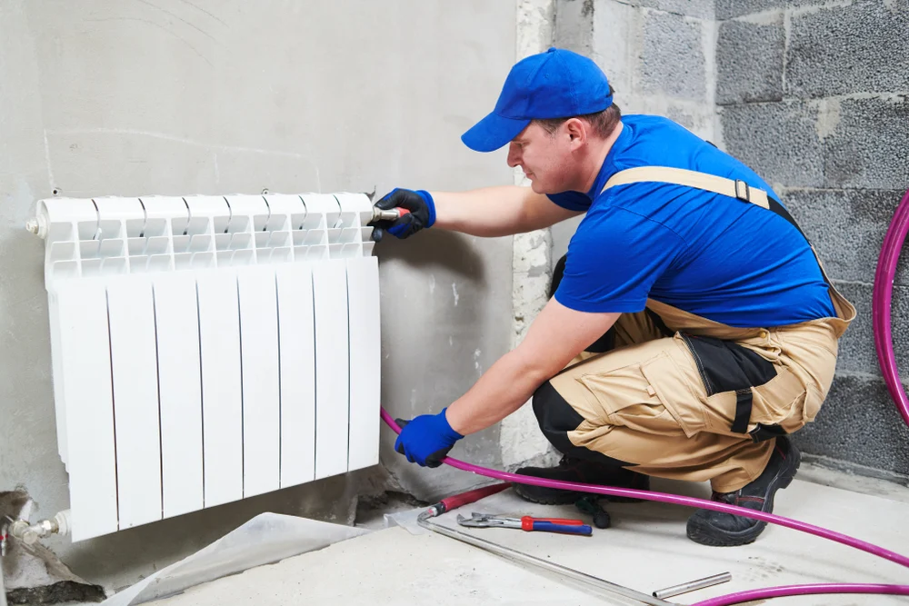 instalator care monteaza un calorifer intr-un spatiu aflat in renovare
