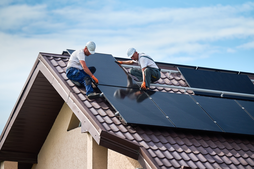 doi instalatori monteaza panouri fotovoltaice pe acoperisul unei case