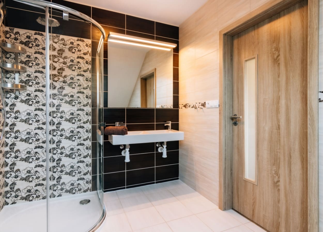 baie moderna cu design contrastant, finisaje ceramice in nuante deschise si inchise, dus cu usi din sticla si accente florale pe faianta