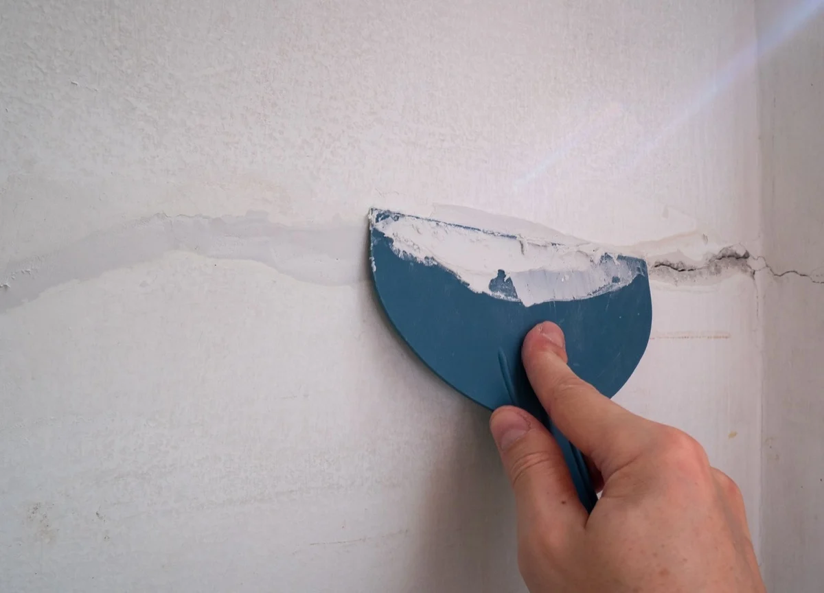 barbat care foloseste o spatula si chit pentru repararea fisurii din perete