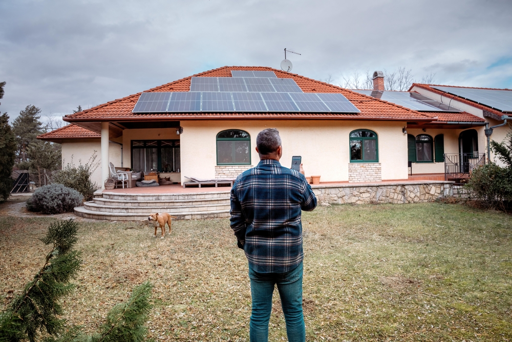 Bărbat care monitorizează pe telefon producția panourilor fotovoltaice de pe acoperișul casei